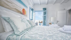 A bedroom with a large bed, a view of the sea through an open door, and a bathroom with a mirror and towels. - Aegean Sea Villas (Astypalaia)