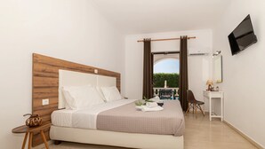 A bedroom with a bed, bedside table, chair, desk, TV, and a view of the outdoors. - Alterego Studios (Zakynthos)