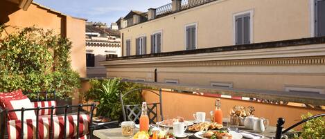 A balcony with a table set for breakfast, including plates of food, drinks, and a basket of bread.