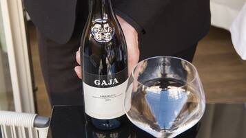 A person holding a wine bottle labeled 'GAJA' next to a wine glass on a reflective surface.