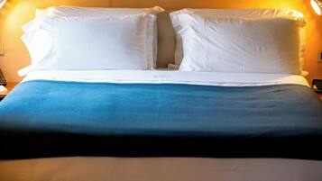 Un letto rifatto con cuscini bianchi e una coperta blu, una lampada da comodino e un telefono ben visibile.