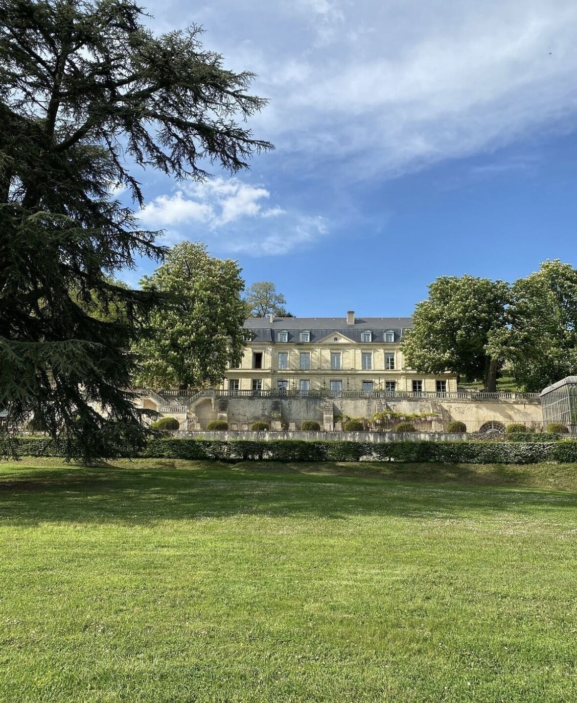 A large, historic building with a symmetrical facade, a central entrance, and a well-maintained lawn in the foreground.