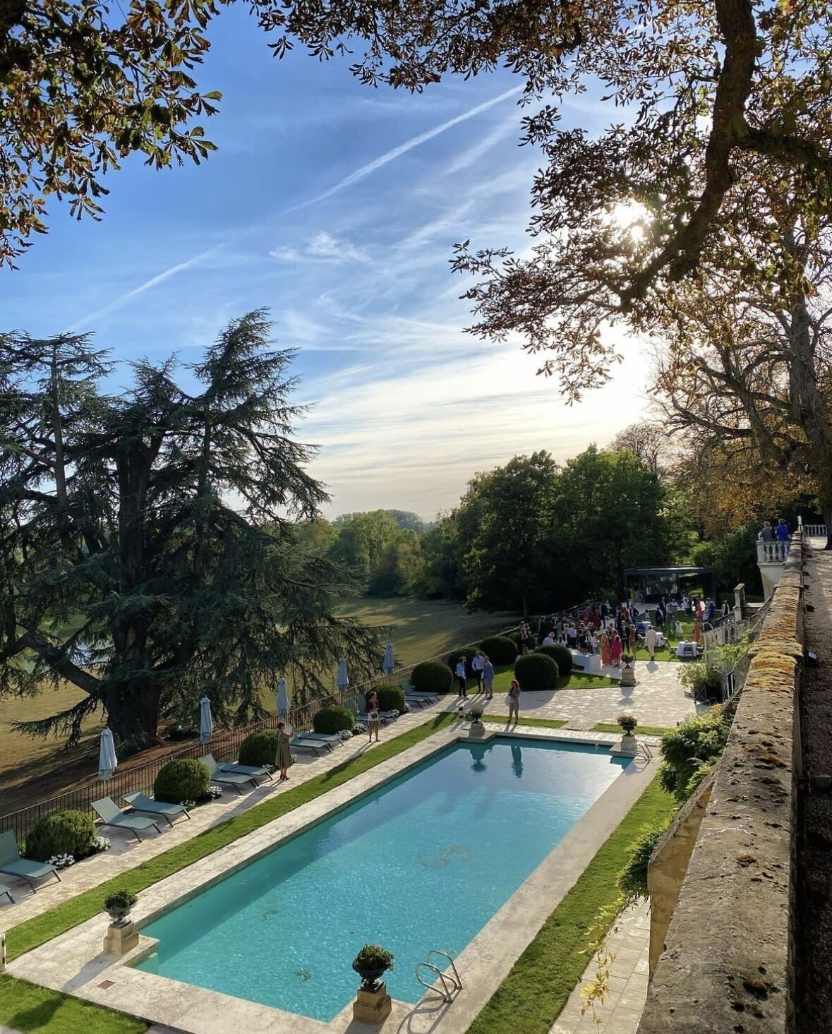 Piscina con sillas de descanso, rodeada de árboles y césped.