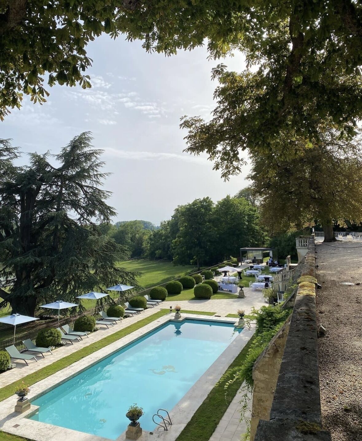 A rectangular pool with a stone border, surrounded by a well-manicured lawn and several lounge chairs.