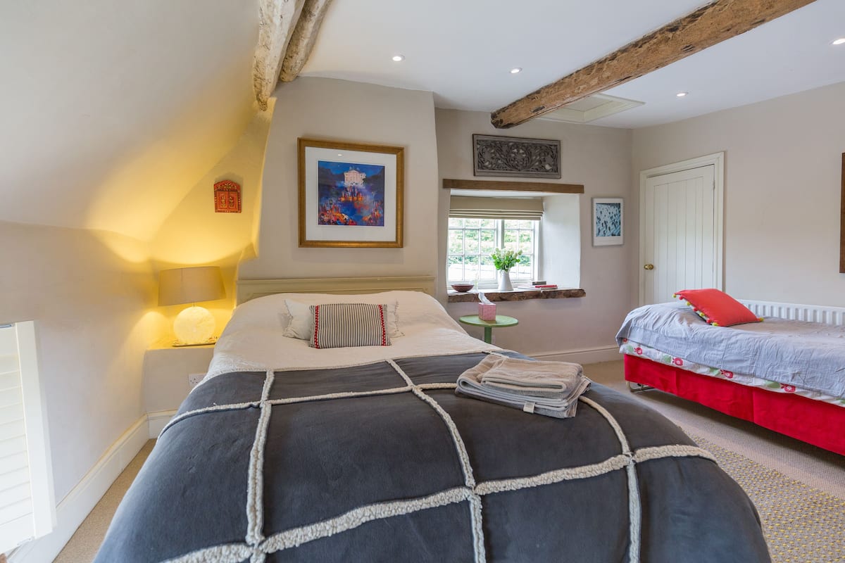 Een slaapkamer met een groot bed, een kleiner bed, een nachtkastje, een lamp, een raam en een deur.