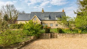 A stone house with a gravel driveway, surrounded by greenery and a stone wall. - Church End Cottage (Newport Pagnell)