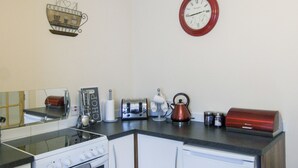 Eine kleine Küche mit Herd, Backofen, Kühlschrank und einer Wanduhr.