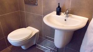 A bathroom with a toilet, a sink, and a hand soap dispenser.
