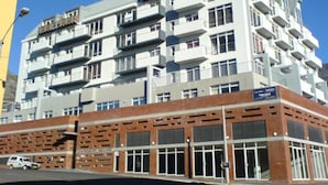 A multi-story building with a brick base and white upper floors, featuring balconies and large windows.