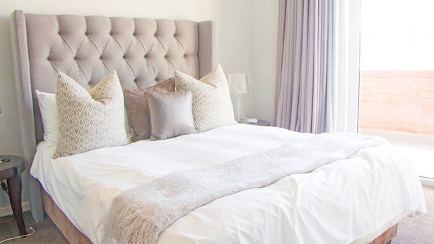 A neatly made bed with a tufted headboard, multiple pillows, and a throw blanket.