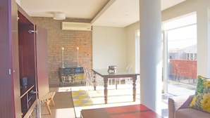 A room with a brick wall, a dining table, chairs, a sofa, and a window with a view of buildings.