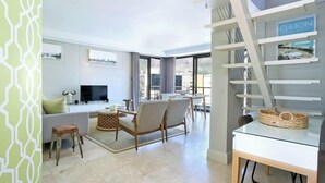 Un salón moderno con televisor de pantalla plana, asientos cómodos y una escalera que lleva a un balcón.