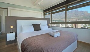 A hotel room with a large bed, a nightstand, and a view of the city.
