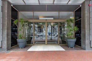 A modern building entrance with glass doors, potted plants, and a tiled floor.
