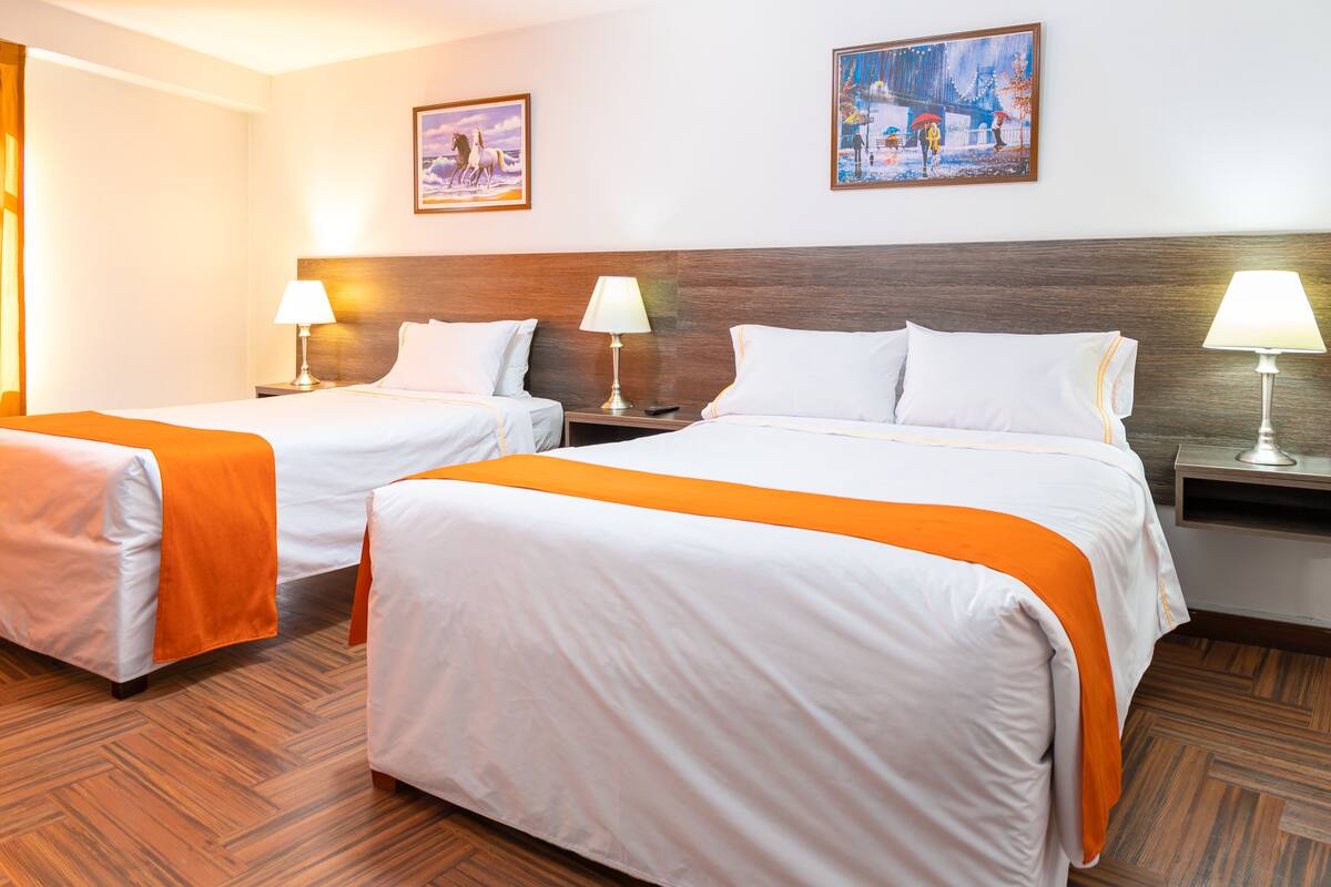 A hotel room with two beds, each with white bedding and orange accents, wooden headboards, and bedside tables with lamps.