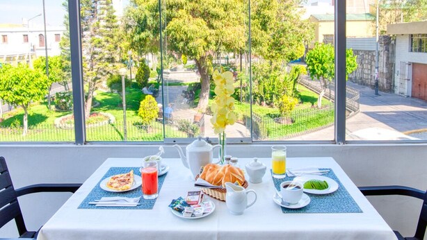Une table de petit-déjeuner dressée avec une variété d’aliments et offrant une vue sur un jardin grâce à de grandes fenêtres.