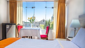 Une chambre d’hôtel avec un lit, une table, deux chaises, une lampe et une vue sur un immeuble par la fenêtre.