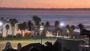 A coastal view with palm trees, a soccer field, and a building with lights. - Vetho Villa (Cape Town)