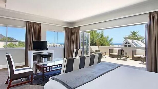 A hotel room with a large bed, a TV, a desk, and a balcony with a view of the beach. - Vetho Villa (Cape Town)