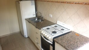 Una cocina pequeña con estufa a gas, lavamanos y refrigerador.