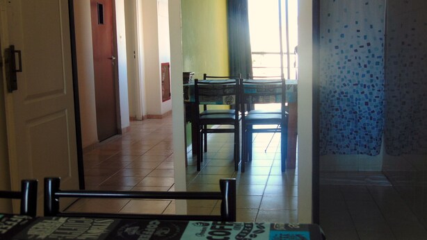 Un pasillo con zona de comedor, una puerta y un ventanal con cortinas.