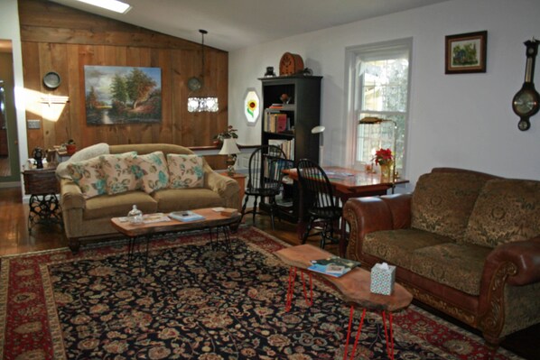 A living room with a sofa, coffee table, and chairs, a bookshelf, and a painting on the wall. - Carriage Corner Bed & Breakfast (Gordonville)