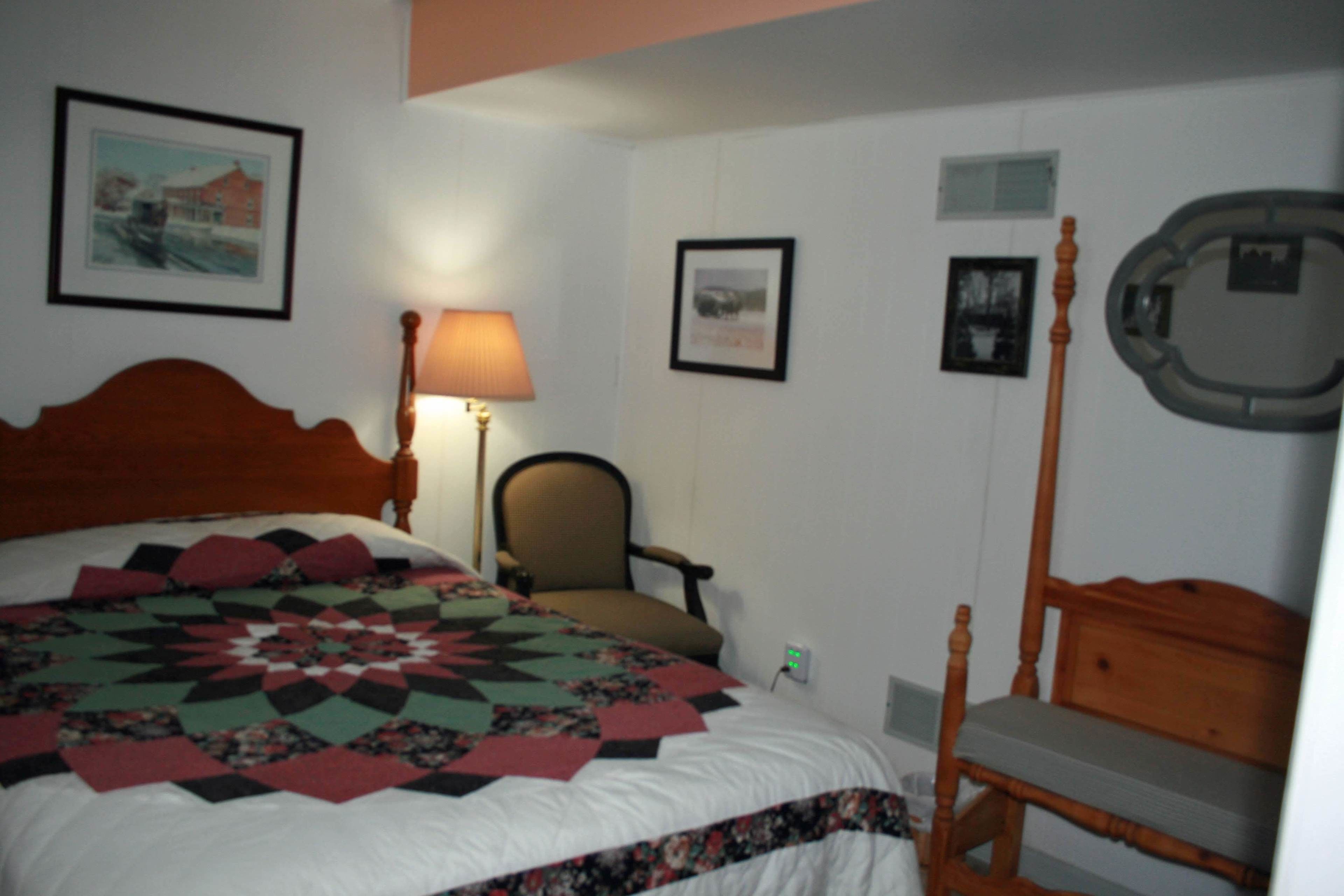 A bedroom with a bed, a chair, a lamp, and framed pictures on the wall.