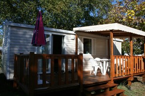 A wooden deck with a covered seating area and a small white building with a window. - Rêve en famille (Gastes)