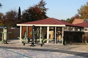 An outdoor gym area with exercise equipment, a covered pavilion, and a gravel ground. - Rêve en famille (Gastes)