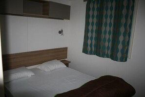 A single bed with a wooden headboard, a bedside table, and a wall-mounted light fixture. - Rêve en famille (Gastes)