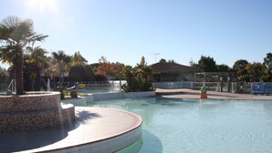 A swimming pool with a tiled deck, surrounded by palm trees and a fence. - Rêve en famille (Gastes)