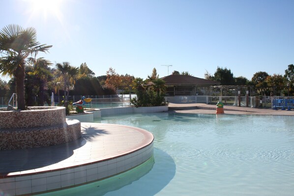 A swimming pool with a tiled deck, surrounded by palm trees and a fence. - Rêve en famille (Gastes)