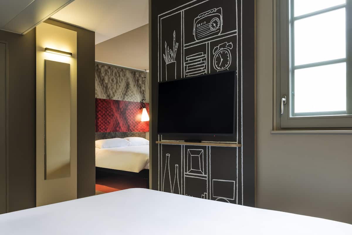 A hotel room with a bed, a TV, a wall with chalkboard drawings, and a window.