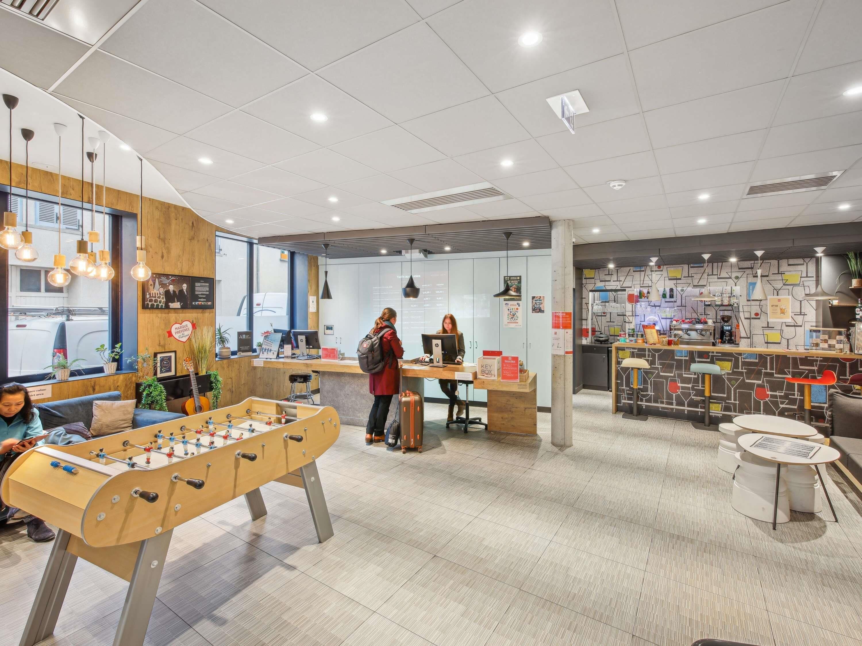 Een moderne hotellobby met een tafelvoetbaltafel, een receptiebalie en een bar.