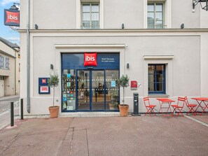 A hotel entrance with a red 'ibis' sign, glass doors, and a small window to the right. - ibis Saint Germain en Laye Centre (Saint-Germain-en-Laye)