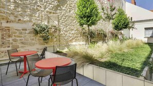 An outdoor patio with stone walls, a red table, and black chairs. - ibis Saint Germain en Laye Centre (Saint-Germain-en-Laye)