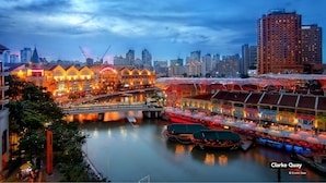 A riverside hotel with a bridge, illuminated buildings, and a city skyline in the background. - ZEN Rooms People's Park Complex (Singapore)