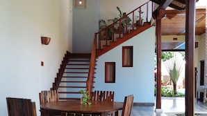 A spacious dining area with a wooden table and chairs, a staircase with a wooden railing, and a checkered floor. - Hotel con Corazón (Granada)