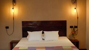 Cama bem arrumada com um edredom colorido, uma cabeceira de madeira e duas luminárias de cabeceira de cada lado.