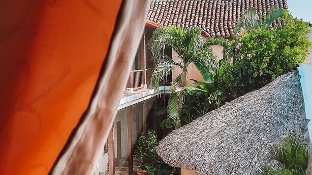 A view of a swimming pool area with a thatched-roof structure, blue lounge chairs, and a tiled roof. - Hotel con Corazón (Granada)