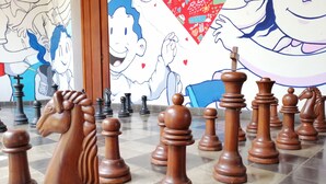 A chessboard with wooden pieces on a tiled floor, set against a wall with colorful murals. - Hotel con Corazón (Granada)