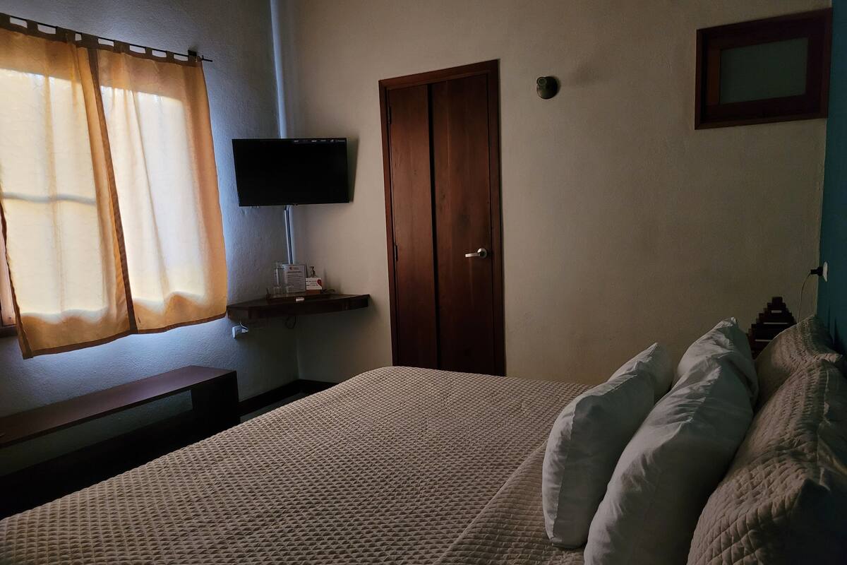 A bedroom with a bed, a TV mounted on the wall, a wooden door, and a window with curtains.