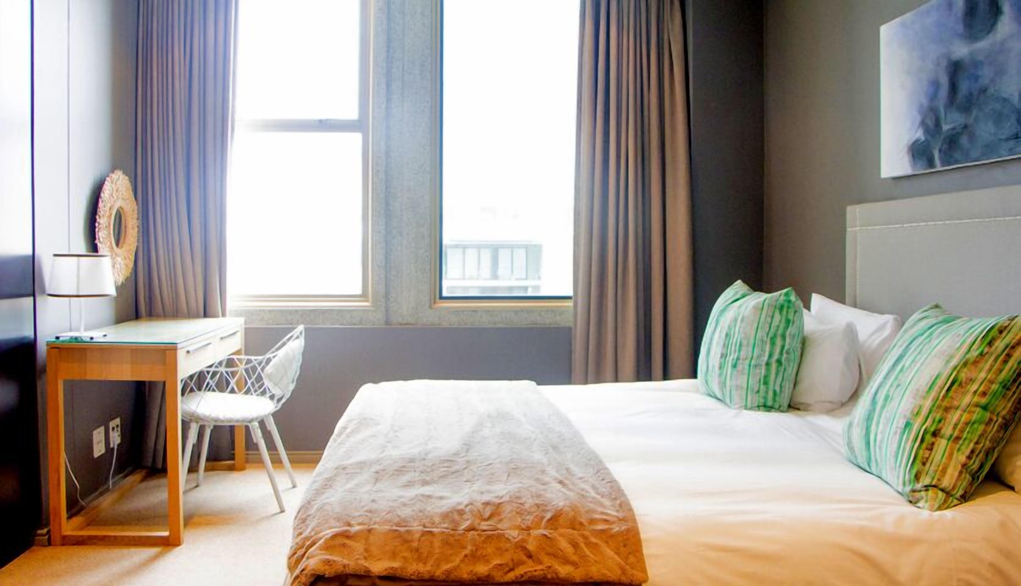 A hotel room with a bed, a desk, a chair, and a window with curtains.