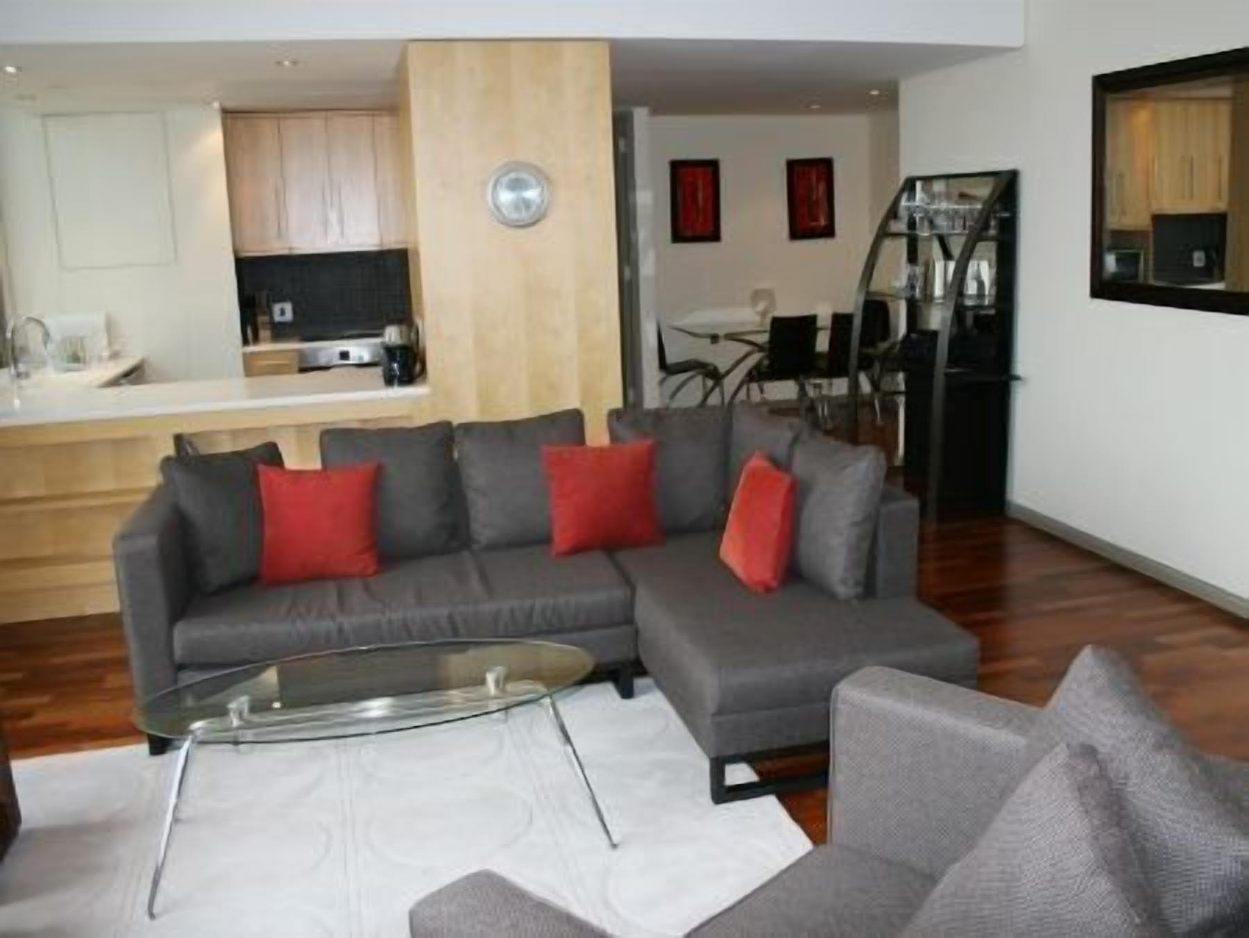 A modern living room with a grey sectional sofa, a glass coffee table, and a white rug.