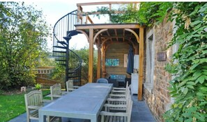 Un espacio al aire libre con techo, que incluye una escalera espiral, una mesa larga y sillas.
