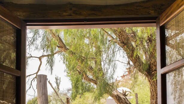 Porta aperta che dà su un patio con un'amaca, una sedia e un muro in pietra.