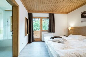 A bedroom with a wooden ceiling, a large window with curtains, a bed with pillows, and a nightstand with a lamp. - Chalet in Wald near Zillertal Arena (Wald-Königsleiten)