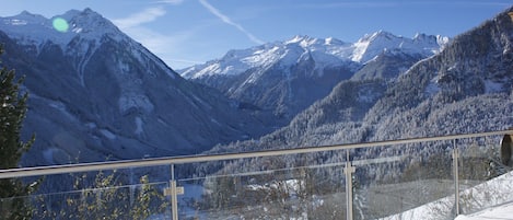 A snow-covered mountain landscape with a clear sky and a glass barrier overlooking a valley.