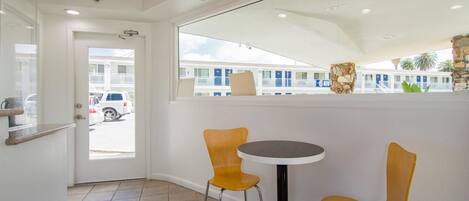 A small room with a white door, a window, a round table, and two yellow chairs.