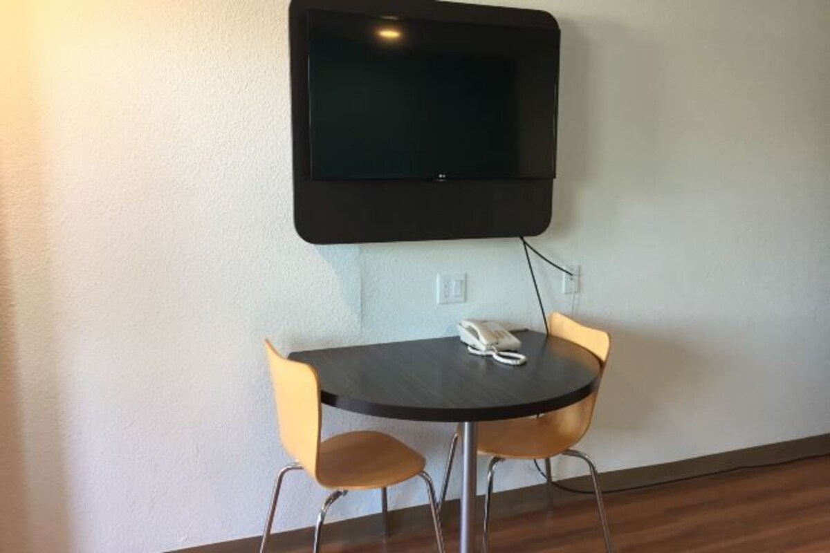 A room with a round table, two chairs, a mounted television, and a telephone on the table.